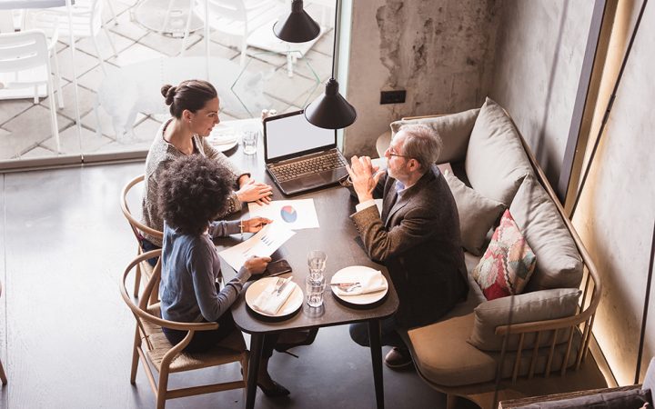 Two female colleagues having business meeting in high end restaurant with senior client. Multi-ethnic group. High angle view