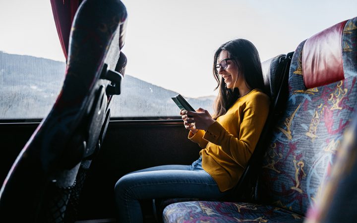 Young beautiful Caucasian woman reading news or checking social media on smartphone while traveling by bus.