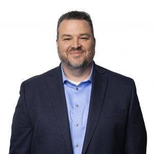 Image shows Buddy Bayer, Colt's Chief Operating Officer, in a dark suit and blue shirt